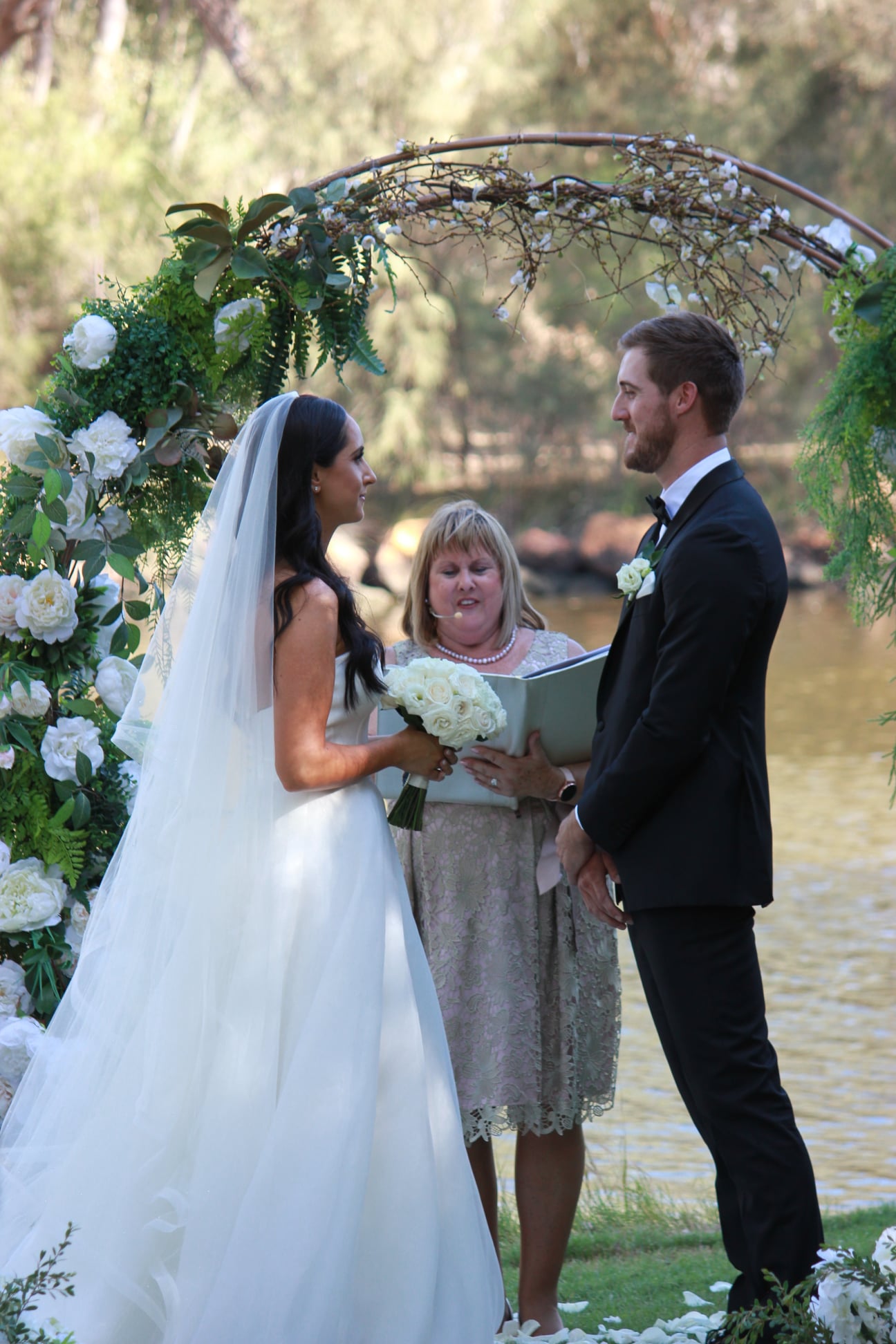 Julie marrying Mady and Ben beneath a floral arch by the river