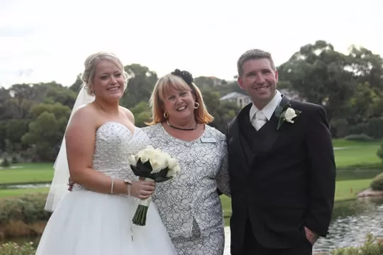 Julie standing between a smiling bride and groom on a lawn