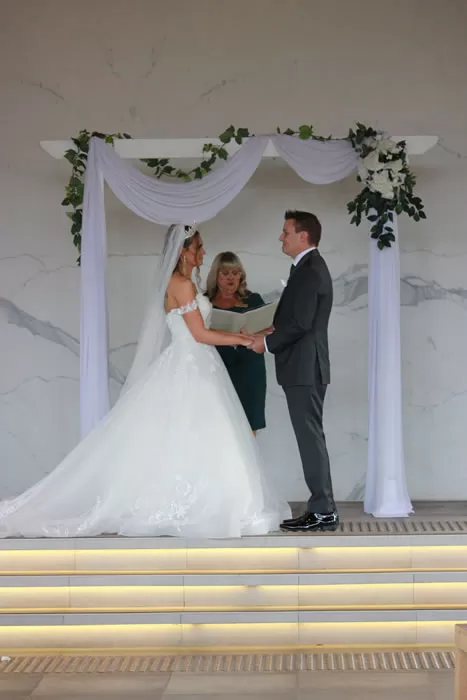 A couple exchanging vows under a draped arbour with Julie officiating