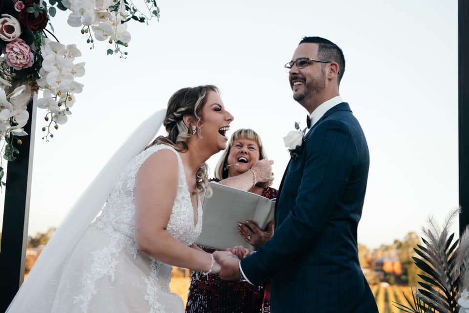 A bride and groom laughing with Julie during their ceremony