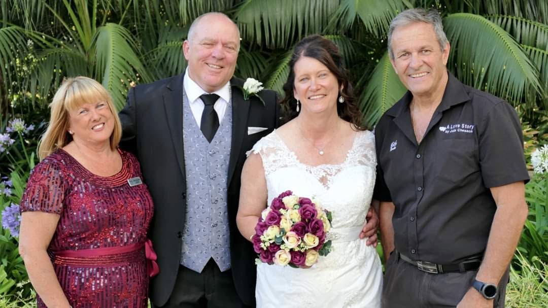 Julie, Michael, Susan and Keith smiling together at a wedding among tropical palms