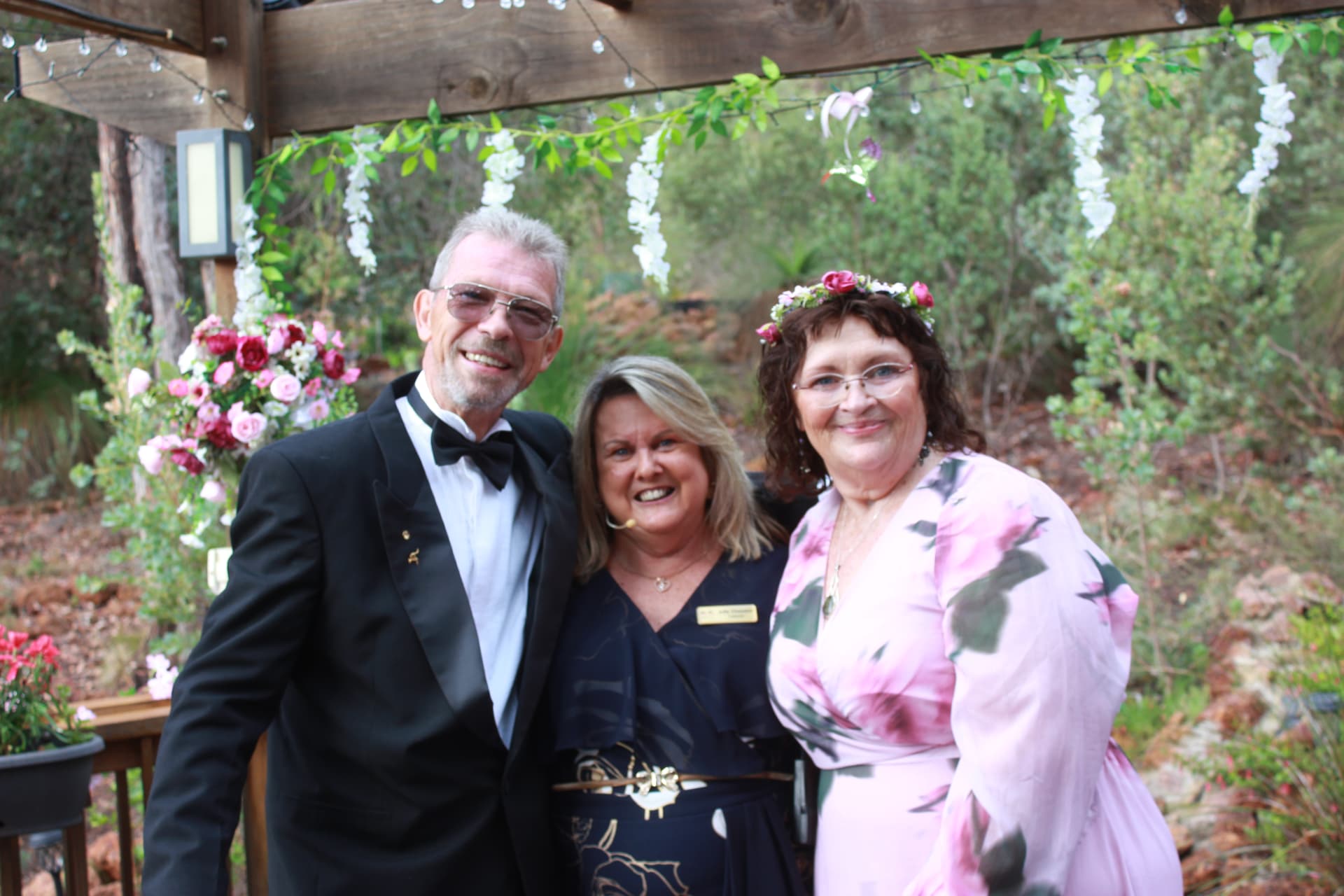 Julie with a smiling couple beneath a flower decorated pergola