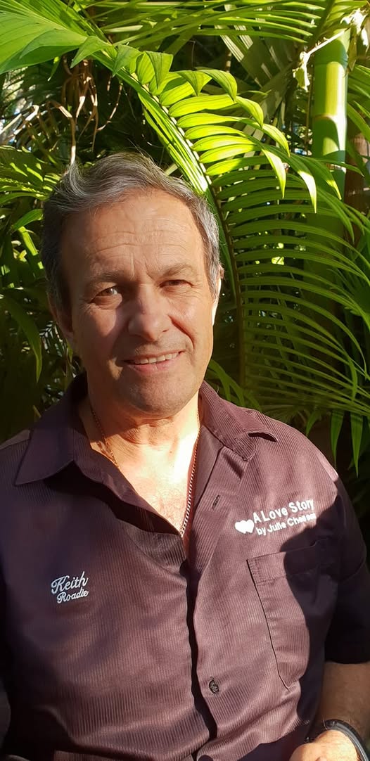 Keith smiling in front of lush tropical palm foliage